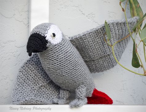 Crocheted African grey parrot amigurumi sitting on an outdoor trellis. Made by Noelle Oguri.