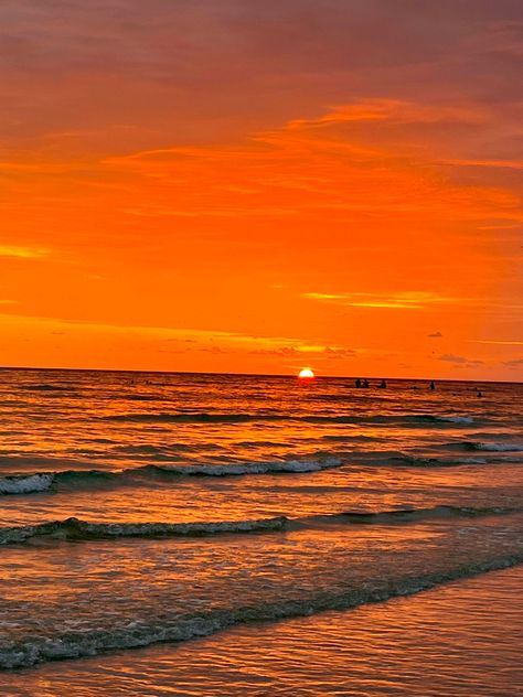 A view of the sunset at the shore from the beach. The sky is a bright orange with half of the sun still shining. Soft waves are flowing onto the shore. The waves have a bit of the orange reflected onto them from the sunset. Orange Ocean Aesthetic, Golden Hour At The Beach, Orange Beach Aesthetic, Orange Sunset Beach, Ocean At Sunset, Pretty Sunsets, Ocean Surf, Orange Sunset, Sky Pictures