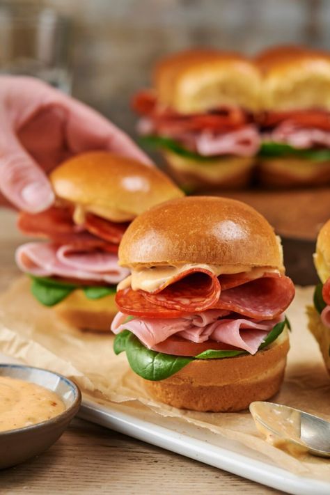 A close-up of brioche slider rolls filled with meats on a wooden board, with a hand picking one roll up. Mini Brioche Sandwiches, Salami Lunch Ideas, Mini Sliders Recipe, Deli Ham Recipes, Brioche Sliders, Mini Subs, Brioche Sandwich, Engagement Food, Cocktail Contest