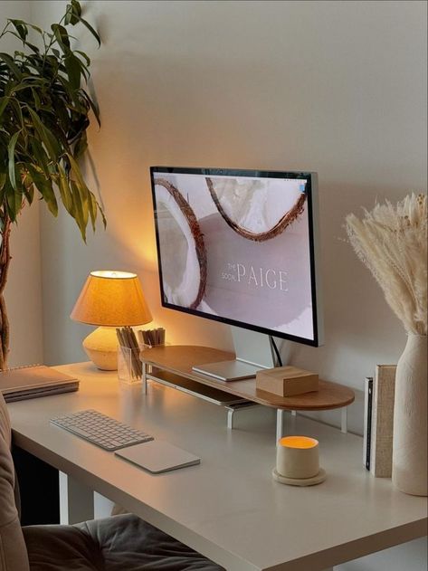 A cozy home office featuring a minimalist desk setup with neutral colors, warm lighting from a small lamp, a wooden monitor stand, and green plant decor, creating an elegant and serene workspace. White Desk Setup, Cozy Desk, Cozy Office, Study Desk Decor, Cozy Home Office, Therapy Office Decor, Aesthetic Space, Warm Lighting, Office Room Decor