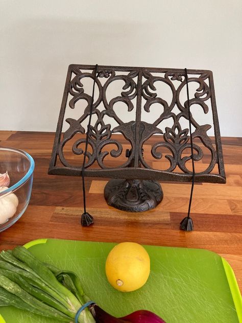 This is a stylish and ornate cook book stand for the kitchen. It is perfect for keeping your page whilst following a receipe. The stand is made from cast iron and has an elegant heart design. The receipe stand has a rustic brown finish with a tinge of black. Two weighted cords hold your page open. Measures: (h) 24 x (w) 26 x (d) 13 cm Recipe Book Holder In Kitchen, Cook Book Display Ideas, Cook Book Holder, Cookbook Display, Cottage Goth, Goth Kitchen Decor, Recipe Book Stand, Thrifted Furniture, Cast Iron Kitchen