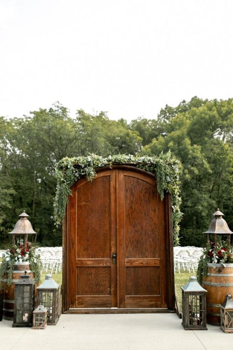 Enchanting outdoor wedding entrance to ceremony with beautiful fall florals and lanterns surrounding gorgeous wooden doors. Wedding Doors Outside Outdoor Ceremony, Wedding Outdoor Doors, Outdoor Ceremony Entrance, Wedding Door Entrance Outside, Outdoor Ceremony Entrance Ideas, Wedding Entrance Outdoor Ceremony, Outdoor Wedding Bride Entrance, Outside Wedding Doors Entrance, Weeding Decoration Outdoor Ceremony