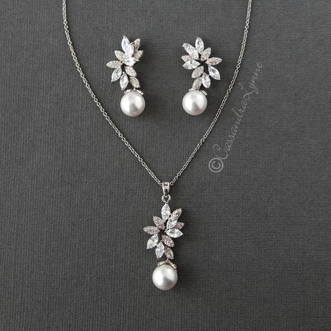 This statement style pendant and earrings set features a 10 mm off-white pearl hanging from a cluster of marquise leaf CZ and micro pave leaf shapes. On a 16 inch chain with a 2 inch extender, the pendant is 1.75 inches long, and the earrings are 1.5 inches with post pierced backs. Rhodium plated, grade AAA CZ, nickel and lead free. Pearl And Diamond Necklace Wedding, Diamond Jwellary, Pearl Necklace And Earring Set, Diamond Necklace Wedding, Diamond Pendant Jewelry, Artistic Earrings, Diamond Pendants Designs, Pearl And Diamond Necklace, Diamond Necklace Designs