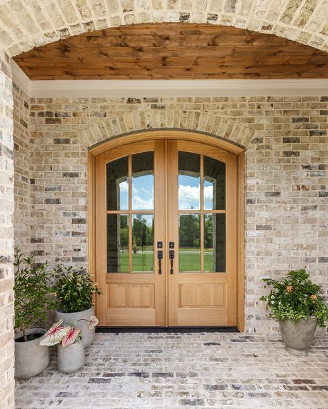 A grand entrance begins with a beautiful front door. This stunning arched double door, stained to match the rich wood ceiling of the front porch, sets the tone for the entire home. It’s the perfect blend of elegance and warmth, welcoming guests with style from the very first step. Arch Front Door Exterior Farmhouse, Round Double Door, Arch Front Porch Entrance, Staircase By Front Door, Rounded Front Door Entrance, Arched Wood Front Door, Arched Double Front Doors, House Doors Front Entrance, Curved Front Door