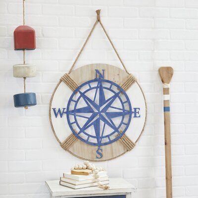 Add some style to your wall with this unique lifesaver wall decoration with a middle compass that will provide a fine decoration worth to your place. Create a balanced space in the most creative way with this expertly crafted wall décor for a captivating focal point. Place this on any blank wall space adding both texture and depth to your home. This item comes shipped in one carton. Item comes with a burlap rope at the top for easy and secure hang. | Longshore Tides Wood Ship Wheel Wall Decor in Decor With Ropes, Compass Wall Decor, Wall Decor Crafts, Nautical Wall Decor, Ship Wheel, Nautical Wall, Blue Wood, Round Decor, Nautical Decor