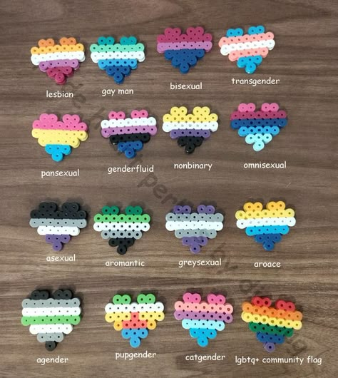 four by four rows of lgbtq+ flags made from perler beads in the shape of hearts on a wooden table as a background, from left to right these are the flags : lesbian, gay man, bisexual, transgender, pansexual, genderfluid, nonbinary, omnisexual, asexual, aromantic, greysexual, aroace, agender, pupgender, cat gender and the general lgbtq+ community flag. Kandi Cuff Ideas, Cat Gender, World Of Wearable Art, Asexual Aromantic, Hamma Beads Ideas, Kandi Cuffs, Diy Kandi Bracelets, Easy Perler Bead Patterns, Pearl Beads Pattern