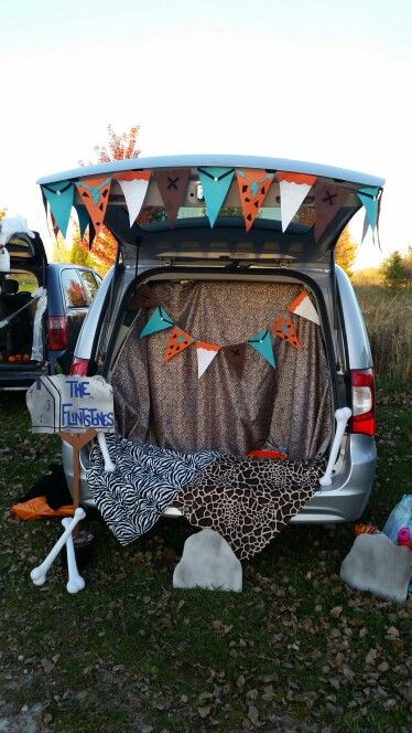 Flintstones trunk-or-treat! The bunting was made from felt, glue and thread. The fabric was pinned/tapped in. The rocks and mailbox were made from paint and cardboard! The bones were store bought. Only wish we had a fake fire for light (or real as it got cold!) Halloween Town Trunk Or Treat Ideas, Flinstone Trunk Or Treat Ideas, Flintstones Trunk Or Treat Ideas For Cars, Car Halloween Costumes Trunk Or Treat, The Flintstones Trunk Or Treat, Flinstones Trunk Or Treat Ideas For Cars, Diy Trunk Or Treat Ideas For Trucks, Trunk Or Treat Family Costumes, Trunk Or Treat Ideas For Trucks Church