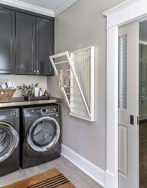 A black front loading washer and dryer sits beneath a gray countertop mounted under glossy black cabinets. Stainless Steel Washer And Dryer Room Ideas, Grey Washer And Dryer Laundry Room, Laundry Room With Gray Washer And Dryer, Gray Washer And Dryer Laundry Room, Grey Washer And Dryer, Gray Washer And Dryer, Pull Down Drying Rack, Cabinets Over Washer And Dryer, Cabinets Above Washer And Dryer