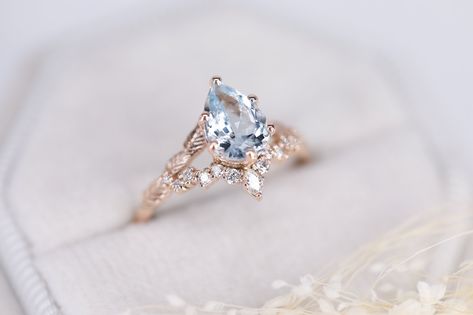 Engagement ring with a gorgeous blue aquamarine. The pear shaped aquamarine is surrounded by VS clarity sparkling white diamonds. The setting is supported by very finely chiselled leaves.The detailed specification are mentioned below.Main stone: AquamarineDimensions: 8mmx6mm Shape: PearSide stones: White diamonds round 1mm(4), 1.2mm(6),1.4(2), marquise 3x1.5 mm(1).Diamond spec: VS clarity, color G-H, conflict freeMaterial: 14K yellow, rose and white goldAvailable sizes: USA 3 - USA 9 (larger and Luxury Delicate Gemstone Wedding And Engagement Rings, Light Blue Aquamarine Diamond Wedding Ring, Wedding Rings With Rose Cut Diamonds And Aquamarine, Light Blue Diamond Ring With Accent Stones For Wedding, Light Blue Diamond Ring For Wedding, Marquise Cut Blue Topaz Wedding Ring, Pear-shaped Blue Topaz Ring For Wedding, Pear-shaped Blue Topaz Wedding Ring, Engagement Ring Aquamarine