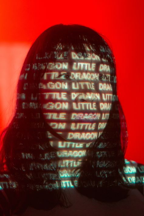 Frontwoman Yukimi of the band Little Dragon standing front of a red backdrop. The Words "Little Dragon" are projected on her face Light Projector Photoshoot, Photo Shoot With Projector, Plexiglass Photoshoot, Photography With Projector, Photoshoot With Projector, Pandora Photoshoot, Projecter Photoshoot, Projector Photoshoot Background, Cheap Dopamine