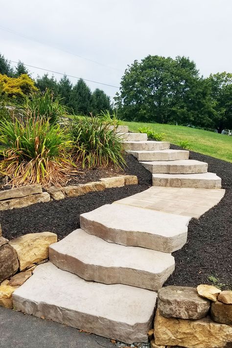 We designed and installed these stone steps that connected a driveway to an upper porch entrance area. Built into the existing slope of a hill, the landing areas between the steps incorporate smaller pavers with a stylish laying pattern. Steps and walkways are landscape elements that offer a great chance to express your unique style and enhance nature's beauty. Landscaping Stone Steps, Sloped Front Yard Steps, Landscape Ideas For Sloping Backyard, Outdoor Steps On A Slope Hill Landscaping, Patio Built Into Hill, Landscape Steps On A Hill, Natural Steps On Hill, Outdoor Landscape Steps, Garden Steps Ideas On A Slope