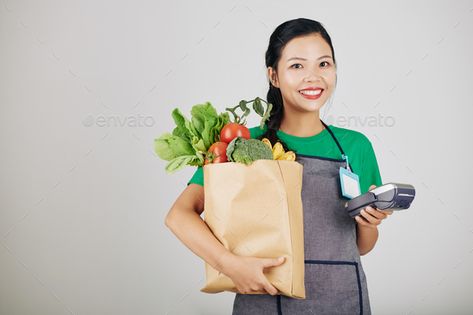 Young female supermarket worker by DragonImages. Pretty smiling young female supermarket worker holding paper package with food and payment therminal #Sponsored #DragonImages, #Pretty, #smiling, #worker Retail Worker, Holding Paper, Dragon Images, Travel