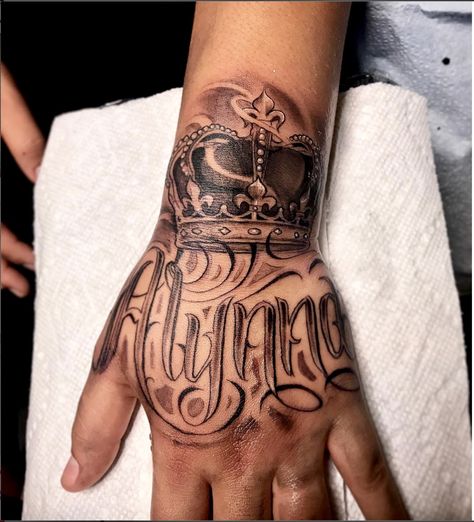 Amazing artist Jorge Jamaica @jamaica.tatts awesome crown hand script tattoo! #jorgejamaica #jorge #jamaica  #renaissance  #ink #3d  #tattoos #tattoo  #amazing  #lettering  #portraits #arm #blackandgrey #crowntattoo #scripttattoo #photorealism #crown  #amazing  #la #handtattoo #hand #fresh #calligraphy #art #artwork #europe #portrait  #script #west Crown Hand Tattoo Men, Hand Name Tattoos For Guys, Hand Tattoo Name, Hand Script Tattoo, Crown Tattoo On Hand, Name Hand Tattoos, Kid Name Tattoo Ideas Mothers, Crown Hand Tattoo, Hand Tattoos Pictures