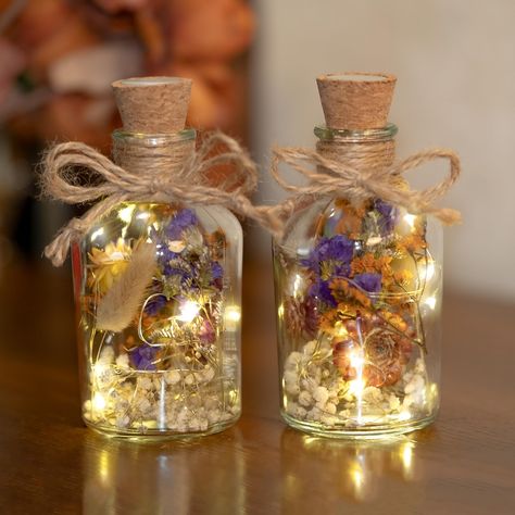 PRICES MAY VARY. Flower Bottles With Fairy Lights: 2 Pack glass bottles with fairy lights dried flowers are has a unique design. Inside the glass bottle, there is a string of lights and it is filled with fragrant dried flowers. The bottle are adorned with decorative hemp ropes tied with a bow. The length of the light string is 1 meter, containing 10 small light bulbs, resembling sparkling stars, emitting a soft and warm glow that illuminates the entire glass bottle. Natural dried flowers: We used naturally dried and scientifically preserved, without harmful chemicals and irritating odors, it’s high quality which can be kept for 2~3 years.The dried flowers in the bottle retain their natural vibrant colors. And also it has a natural smell that makes you feel relaxed. Lighting Modes: Bottle s Glass Bottle Centerpieces, Cocktail Table Centerpieces, Cottage Core Home Decor, Cottage Core Wedding, String Lights Inside, Table Decorations Wedding, Bottle Centerpieces, Flower Bottle, Decorated Bottle