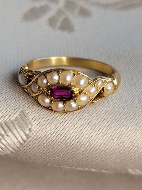 Originally from England and purchased from a London estate auction, this antique natural ruby and multi-pearl ring is sweet and unique. The setting has an unusual twist of pearls surrounding a faceted natural red ruby with openwork shoulders to either side. The design of the setting almost resembles an eye or a serpentine design. This little pretty dates back well over 140 years into Victorian times but it could be mistaken for a Tudor or Elizabethan ring from its design.  The scrollwork on the Pearl And Ruby Ring, Vintage Rings Antiques, Marathi Jewellery, London Estate, Stylish Gold Earrings, Victorian Rings Vintage, Vintage Ruby Ring, Antique Gemstone Rings, Ruby And Pearl