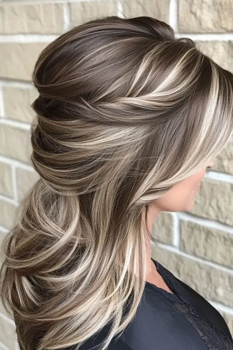 Woman with long, layered hairstyle featuring blonde highlights against a brick wall background. Best Hair Color To Camouflage Gray, Brown And Blond Highlight, Fresh Hair Color Ideas Brunettes, Mocha And Blonde Highlights, Hair Color Ideas For Brunettes Going Lighter, Hair Color Options For Brunettes, Partial Highlights For Brunettes Fall, Hair Color Ideas For Greying Hair, Hair Color To Cover Gray Hair