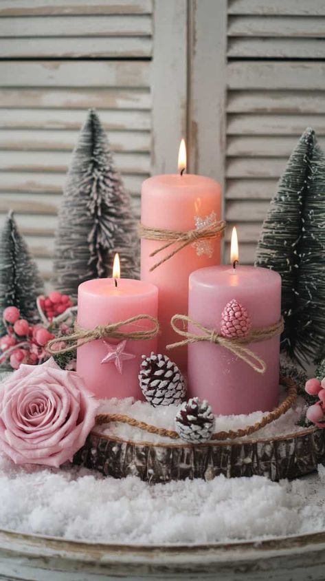 A beautiful and cozy winter-themed arrangement. At the center, there are three pink pillar candles of varying heights, each decorated with twine and delicate holiday ornaments such as pink and silver pinecone-shaped decorations and a small pink star ornament. The candles are lit, casting a warm, soft glow. Pink Christmas Bedroom, Pink Pillar Candles, Pink Shabby Chic Christmas, Christmas Tree Roses, Pink Christmas Table, Champagne Christmas Tree, Pink Xmas Tree, Christmas Candle Centerpiece, Cozy Candle