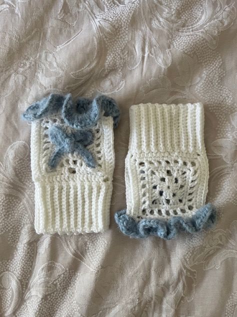 a pair of crocheted fingerless gloves lay next to each other on a beige jacquard weave quilt cover. one is laying the right way round with the front showing while the other is upside down and has the back showing. the glove has a textured blue ruffle trim at the top and a blue bow in the front middle (made using the same yarn). the remainder of the glove is white and the body has a granny square like pattern. the wrist of the glove is ribbed. Hand Warmer Crochet Pattern, Cute Crochet Gloves, White Yarn Crochet Ideas, Hand Warmers Crochet Pattern, Fluffy Crochet Projects, Light Blue Crochet Ideas, Crochet Ideas Blue, Blue Crochet Pattern, Croquette Crochet