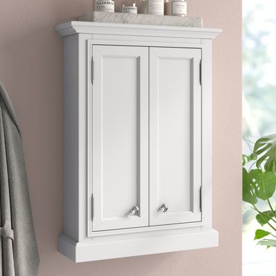 This wall-mounted, 2-door bathroom cabinet saves you space while creating functional storage. It's crafted from solid birch wood in a neutral hue that goes with a variety of color schemes. The design features a rectangular shape with crown molding at the top and picture frame paneling on the cabinet doors. We love that they open to reveal compartments separated with an adjustable shelf - so you can store anything from shampoo to cotton swabs. It's wall-mounted, so it's ideal for just over the to Bathroom Wall Cabinet Above Toilet, Cabinet Above Toilet, Wall Bathroom Cabinet, Wall Mounted Bathroom Cabinet, Kitchen Appliance Set, Wood Wall Bathroom, Wall Mounted Bathroom Cabinets, White Bathroom Cabinets, Organizing Bathroom Cabinets