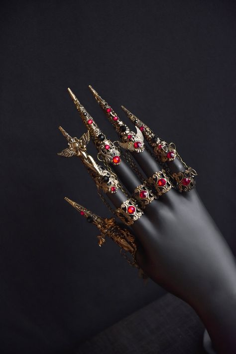 Beautiful gothic claw rings will be a great addition to your look. The photo shows a set of claws and medium rings in old gold color. The claws are decorated with small swords with wings and black and red rhinestones. The middle rings are attached to the claws with small chains.  The set includes 5 long claws and 4 medium rings Suitable for small and medium fingers. Not suitable for very wide fingers Claw rinds is available in different colors (see last photo). Finger Chain Ring, Red And Gold Accessories, Finger Claw Jewelry, Finger Claws, Hand Armor, Claw Rings, Brass Knuckle, Claw Ring, Claw Nails