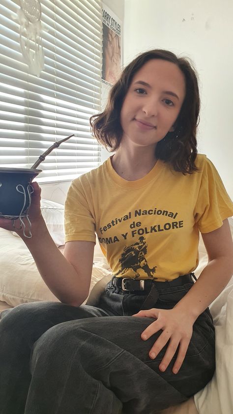 Woman in yellow graphic tee, tucked into black jeans. Sitting drinking maté. Yellow Graphic Tee Outfit, Yellow Graphic Tee, Black Shirt Outfits, Brocade Blouse Designs, Brocade Blouse, Graphic Tee Outfits, Brocade Blouses, Yellow Pants, Concert Festival