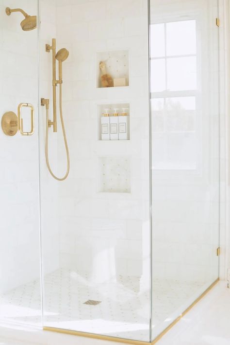 marble shower with glass doors, gold shower fixtures and mosaic shower floor Gold Shower Glass Door, Moen Brushed Gold Shower Fixtures, Gold Shower Fixtures Master Bath, White Shower Gold Fixtures, Moen Shower Fixtures Gold, White Shower With Gold Fixtures, Gold Shower Niche, White And Gold Shower Tile, Shower Fixtures Gold