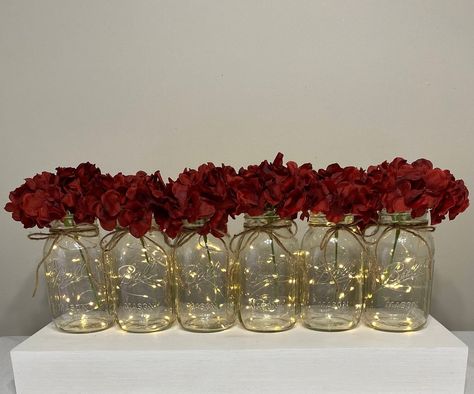 This listing includes 6 beautiful quart mason jars with fairy lights, twine bows and artificial flowers. We have many flower options to choose from. Wine red  Hydrangeas shown in first photo. You can get color ribbon instead of twine, just message us. These lighted mason jars are the perfect wedding table centerpieces and can be used for bridal showers, baby showers or home decor! Quart mason jars are 6.9 inches tall by 3.5 inches wide. The lights have a on/off switch and have replaceable cr2032 Fairy Light Mason Jars, Centerpieces Burgundy, Mason Jars Wedding, Xv Ideas, Gold Wedding Centerpieces, Red Centerpieces, Red Wedding Decorations, Red Wedding Theme, Party Table Centerpieces