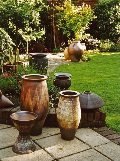 A group of three African inspired decorated planters with sgraffito decoration in the foreground, with a large Ali Baba planter at the top of the image. A group of three Jenifer Jones black pots partially visible on the low brick wall. African Garden Ideas, African Planters, Pot Grouping, African Garden Design, African Garden, Napa Style, African Landscape, African Inspired Decor, Ali Baba