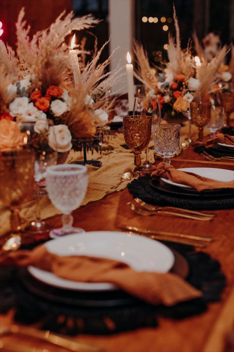 wooden table with black macrame charger, amber and white glass, gold cutlery, terracota napkin and pampas everywhere. Burnt Orange And Brown Wedding Decor, Copper And Black Wedding Decor, Burnt Orange Black And Gold Wedding, Burnt Orange Round Table Setting, Amber And White Wedding, Black White Orange Wedding, Black And Orange Table Setting, Black And Amber Wedding, Rust And Black Wedding Decor