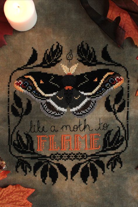 A finished cross stitch pattern of a black moth with orange accents. A stylized black leaf border surrounds the moth. Cursive text reading "like a moth to" is backstitched underneath. The word "flame" is in all caps and is orange. Moth Cross Stitch, Gothic Crosses, Faux Taxidermy, Halloween Cross Stitches, Cross Stitch Rose, Embroidery And Stitching, Cross Stitch Art, Moth, Cross Stitch Embroidery