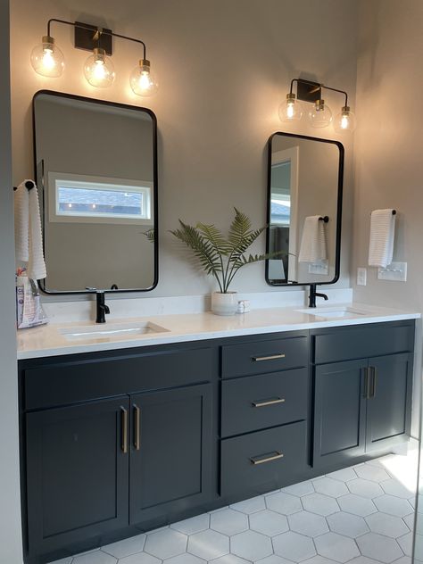 This gorgeous bathroom has painted cabinetry and gold hardware to perfectly team up with the white tile and black light fixtures. Black Floor White Vanity Bathroom, Bathroom Color Schemes Black Hardware, Bathroom Decor Black Vanity, Black And Gold Accent Bathroom, Iron Ore With Black Hardware, Guest Bathroom Ideas Black Vanity, Black White And Brass Bathroom, Restroom Cabinets Ideas Paint Colors, Dark Cabinet Master Bath