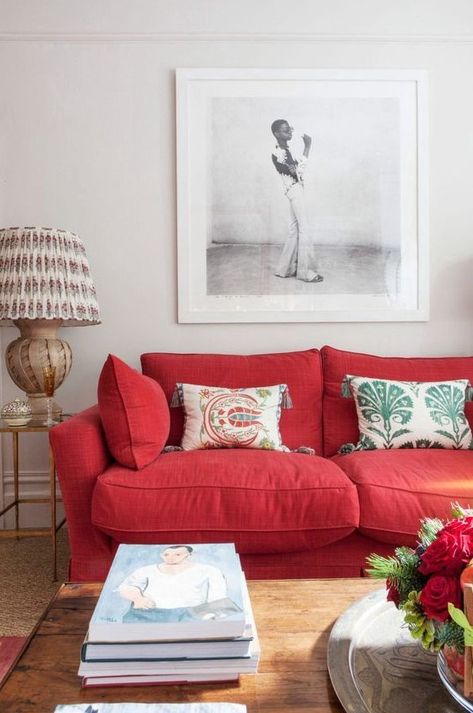 Picture of a modern living room with a bold red sofa, printed pillows, a statement artwork, a printed lamp and stacks of books