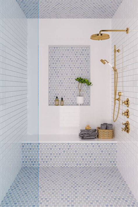 a coastal shower space done with white and blue tiles, a niche, a bench, some towels and gold fixtures Cappuccino Marble Bathroom, Interior Shower Design, Transom Window Shower Master Bath, Modern Coastal Interior Design Bathroom, Bathroom Shower Walk In, Cottage Modern Bathroom, Master Bathrooms With Gold Fixtures, Master Shower Layout, Bathrooms With Color