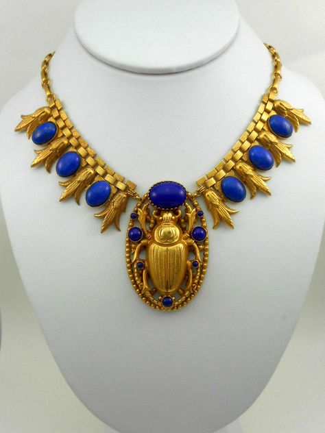 ASKEW LONDON SIGNED OVAL SCARAB AND CABOCHON NECKLACE.   ANTIQUED GOLD PLATED BRASS STAMPING OVAL DECORATED WITH LARGE BRASS STAMPING   SCARAB AND ASST SIZE LAPIS BLUE GLASS CABOCHONS. OVAL IS FLANKED BY LINKS OF FLAT   CHAIN DECORATED WITH BRASS STAMPING LILIES AND LAPIS BLUE GLASS OVAL CABOCHONS. Bug Board, Egyptian Revival Jewelry, Ancient Egyptian Jewelry, Magic Items, Walmart Jewelry, Customizable Jewelry, Coban, Long Pearl Necklaces, Jewellery Sketches