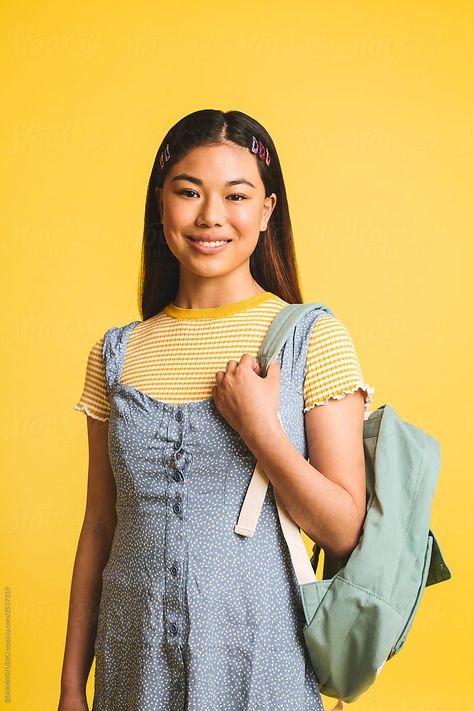 Portrait of a teenager asian girl holding a backpack in front of yellow background. Person Holding Backpack Reference, Holding Backpack Reference Drawing, Wearing Backpack Reference, Backpack Pose Reference, Holding Backpack Reference, Holding Bag Pose, Front Pose Reference, Backpack Pose, Back To School Photoshoot