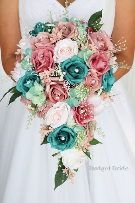 This brides’ bouquet is the perfect option if you have chosen a classic theme for your wedding. A lovely array of dusty rose and mauve are center-stage in this stunning arrangement. This bouquet is made with dusty rose-colored roses, mauve roses, barely pink roses and teal roses all accented by pearls and rhinestones. As always, this bouquet has been wired by hand and designed by our in-house florists - you can rest assured that our bouquets will maintain their quality and stand the test of time Teal Pink And Gold Wedding, Teal And Pink Wedding Bouquet, Teal And Coral Wedding Ideas, Pink And Turquoise Wedding Decorations, Pink And Turquoise Wedding Theme, Rose Gold And Teal Wedding Theme, Teal And Pink Wedding Ideas, Coral And Teal Wedding Bouquet, Rose Gold And Turquoise Wedding Theme