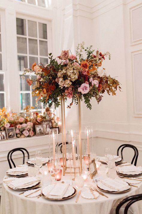 Lush floral meadows surround the cake at this Parisian inspired fall wedding with hues of dusty rose, terra cotta, mauve, copper, and lavender composed of roses, ranunculus, copper beech, clematis, and fall foliage. Design by Rosemary and Finch in Nashville, TN. Terra Cotta Wedding Centerpieces, Black Bistro Chairs, Tall Flower Centerpieces, Copper Beech, Fall Hydrangea, Foliage Design, Dried Hydrangeas, Unique Wedding Flowers, Floral Chandelier