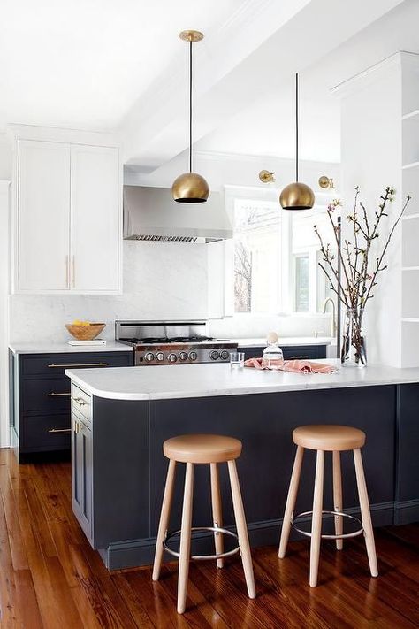 Stunning kitchen features wood floors highlight navy blue lower cabinets and white upper shaker cabinets fitted with long brass pulls and topped with honed white marble countertops as two carmel leather counter stools sit in front of a blue peninsula illuminated by two gold bowl pendants . Model Dapur, Two Tone Kitchen Cabinets, Kitchen Peninsula, Classic Kitchen Design, Kabinet Dapur, Classic Kitchen, Kitchen Farmhouse, Kitchen Cabinet Colors, Classic Kitchens