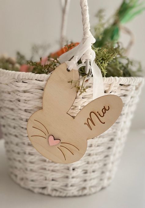 "Personalize this cute wood bunny basket tag with your child's name and choose your favorite heart color. These tags are laser cut and engraved. Choose from 3 heart colors White  Pink Light blue Dimensions: Approximately    3.5\" W x 4\"H  1/8 inch birch  Laser cut and engraved  Wood bunny tag comes with white fabric for hanging on basket (The fabric strip will fray, it is part of the design. You may cut along the edges for a cleaner strip, but it will continue to fray with use.) If you need a custom order please don't hesitate to send me a message. I will try my best to accommodate any requests PLEASE NOTE: The wood grain may vary slightly due to the nature of the product. No two wood pieces are the same in color or grain movement.  Wood has natural defects such as; cracks, dark spots, ho Bunny Pants Basket, Easter Cricut Ideas, Easter Wooden Crafts, Glo Forge, Spring Pottery, Wood Easter Basket, Glowforge Aura, Laser Gifts, Wood Bunny