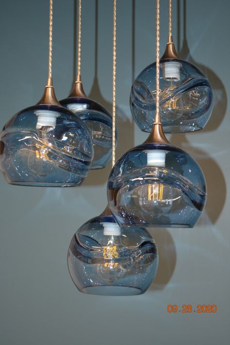 Up close and personal with our Swell 767s in Steel Blue! These hand-blown, eco-friendly glass shades are installed on a custom Five Pendant Cascade Chandelier. Swipe to see the lights on, and check out our website for more information!

#bicycleglass #sustainableliving #artisanmade #madeinusa #lighting #lightingdesign #statementlighting #handblownglass #bathroomlighting #foyerlighting #chandelier #remodel #interiordesign #lightfixtures #globe #pendant Blue Chandelier Dining Room, Blue Glass Light Fixtures, Blue Glass Lights, Blue Hanging Lights, Navy Light Fixture, Blue Glass Pendant Light, Modern Organic Lighting, Blue Pendant Lights, Cascading Chandelier