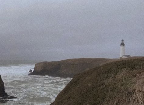 a lone lighthouse sits to the right of the image perched upon rocky cliffs which are covered in brown wintry grass. the sky is gray and foggy, and the ocean crashes against the rocks beneath the lighthouse. the waves are gray and misty. the image gives an aura of both hope and desperation. Rocky Ocean Aesthetic, To The Lighthouse Aesthetic, Foggy Coast Aesthetic, Living By The Sea Aesthetic, Pacific Northwest Gothic Aesthetic, Pacific Northwest Coast, The Coast Aesthetic, Stormy Sea Aesthetic, Pacific Northwest Gothic