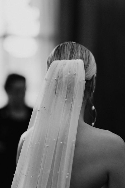 A bride wears a white strapless minimal wedding gown with a sweetheart neckline. Her blonde hair is tied in a low bun over which a long pearl veil is worn. She holds a large bouquet of fluffy white roses. Low Bun Wedding Hair With Veil, Black Tie Aesthetic, Bride Bun, Blonde Bun, Tower Cake, Large Bouquet, Pearl Veil, Decker Bus, Wedding Hairstyles With Veil