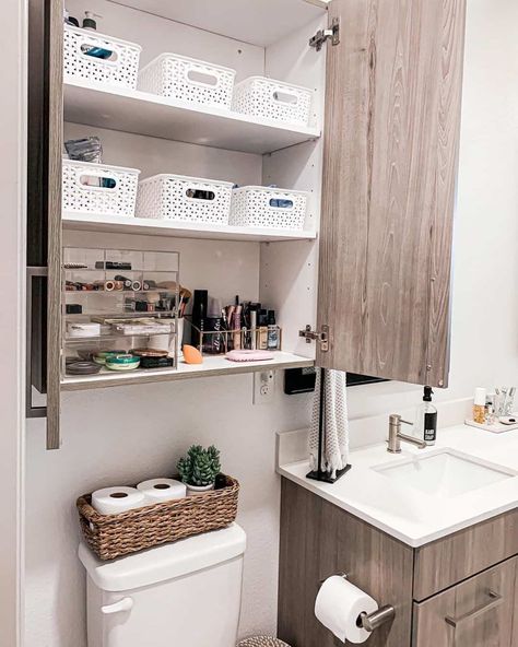 White bins and clear storage trays are used for simple bathroom organization in a wooden cabinet. A coordinating wooden sink vanity creates a cohesive look. Place toilet rolls in a wicker tray to store these items in style. Small Bathroom Cabinet Organization, Simple Bathroom Organization, Wooden Sink, Easy Bathroom Organization, Small Bathroom Cabinets, Bathroom Vanity Organization, Wooden Bathroom Cabinets, Bathroom Cabinet Organization, Bathroom Sink Cabinets