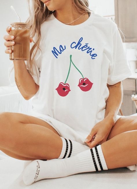 Transport yourself to a quaint Parisian café with our adorable "Ma Chérie" tee. This relaxed-fit cotton t-shirt is perfect for soaking up the summer sun. Featuring charming script that declares "Ma Chérie" (French for "My Darling"), it's accented with playful cherries. French Graphic Tee, Ma Cherie, Parisian Cafe, 15 Gifts, My Darling, Summer Sun, Trending Now, Bridal Accessories, Matching Sets