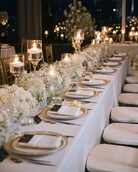 Transform your reception into a regal affair with intricate gold tablescape details. White florals, statement candles and the gold accents create an ambiance of opulent elegance. ✨   #weddingtablescape #tabelscapedesign #weddingreception #weddinginspo #weddingdetails #weddingdecor #weddingstyle #weddingplanner #nycweddings #overthemoon #stylemepretty #luxuryweddings #caratsandcake #alinatoevents White And Gold Wedding Place Setting, Elegant Outdoor Wedding Reception Table Arrangements, White Wedding Design, Gold And White Reception Decor, Classic Elegant Wedding Table Setting, Neutral Wedding Decorations Receptions, Vintage Elegance Wedding, All White Wedding Reception Decoration, Vogue Wedding Decor