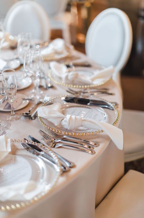 Elegant white and gold wedding place setting with gold ball edge glass charger plate, knotted satin napkin, and silverware at the Liberty Grand. Photo by Sandra Monaco.  #WhiteandGoldPlaceSetting #WeddingPlaceSettingInspiration #WeddingPlaceSettingIdeas #BallEdgeGlassChargerPlate #WeddingGuestTableInspiration #WeddingGuestTableIdeas #TorontoWedding Gold Chargers And Silver Silverware, Charger Plate With Napkin, Gold Charger With Silver Flatware, Gold Rim Charger Plate Wedding Tables, Wedding Flatware Setting, Wedding Place Settings With Charger, Glass Charger Plates Wedding, Satin Napkins Wedding, Silver And Gold Wedding Table