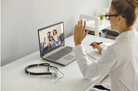 Young female mecical worker in white uniform greeting happy family with child before online consultation on laptop from medical clinic office. Telehealth, telemedicine cocnept Talking On The Phone, On The Phone, The Desk, Girls With Glasses, A Pen, Photoshoot Inspiration, The Office, Stock Images Free, A Table