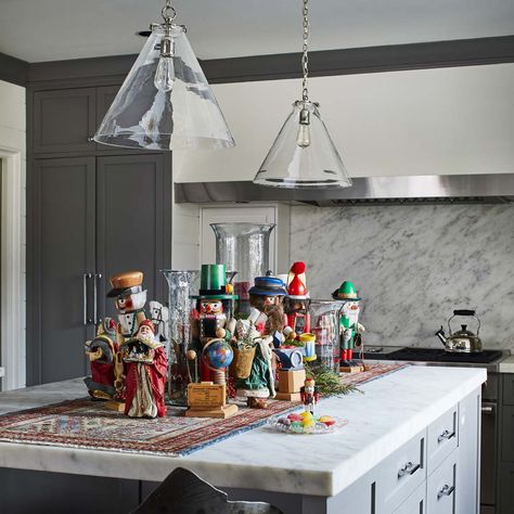 In the kitchen, a marble-top island displays nutcrackers and Santa figurines on a small fine rug. Photography by Laurey W. Glenn Nutcracker Display Ideas, Nutcracker Display, Simple Winter Decor, Nutcrackers Display, Christmas Floral Decor, Holiday Home Tour, Holiday Arrangement, Santa Figurines, Christmas Interiors