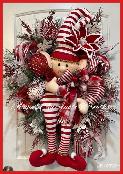 This cutie is created on a 24 inch Evergreen pine base surrounded with 10 inch deck  Taking centerstage is the custom hand zone, beautiful elf and peppermint stripes He is surrounded with beautiful textures of crazy Christmas greenery, shattered proof, ornaments for candy and peppermint rolls throughout and 4 inch wired ribbons from Steven another textures of wired rib This cutie will ship from Texas from pet and smoke free He is approximately 37 inches from top to bottom by 25 inches wide by 10 inches in depth Thank you for looking at my shop love, Angie Popular Christmas Wreaths 2024, Red And Black Buffalo Plaid Christmas Wreath, Elf Tree Topper, Elf Wreaths, Red And White Christmas Wreath, Elf Christmas Wreath, Swag Wreaths, Peppermint Wreath, Rustic Wreaths