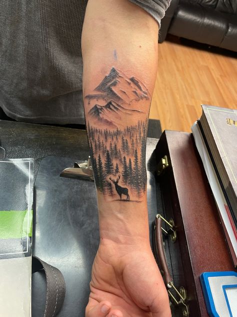 Buck silhouette standing amongst a forest with soaring mountains overlooking. Mountain Men Tattoo, Moutain Tattoos Men Forearm, Elk With Mountains Tattoo, Outdoors Tattoos For Guys, Men Tattoo Ideas Hunting, Outdoor Family Tattoo Ideas, Mountain And Deer Tattoo, Mens Outdoors Tattoo Ideas, Outdoor Tatoos Men